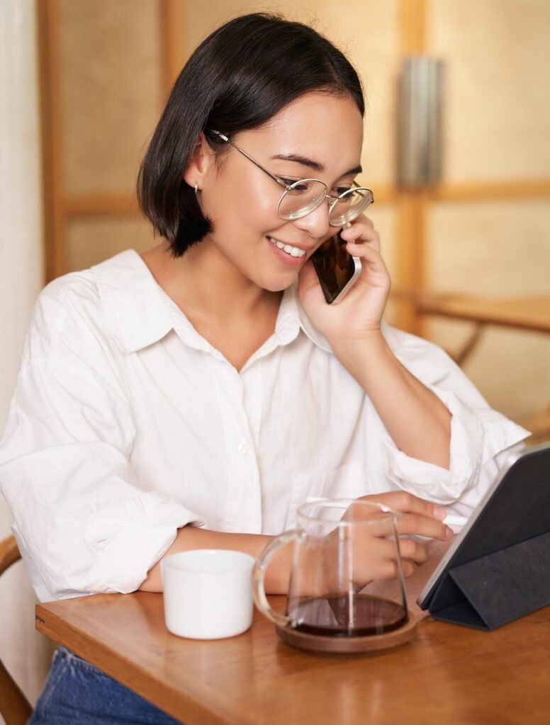 Woman in glasses, answer phone call in a cafe, drinking coffee, looking at work on tablet, working