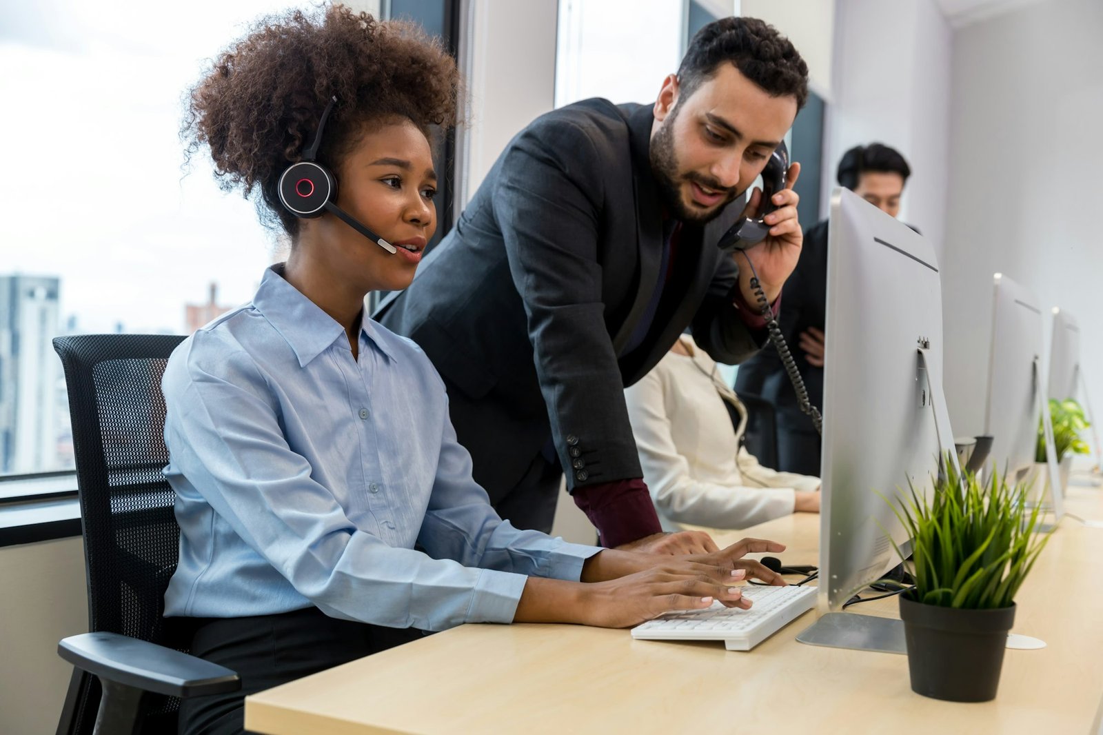 Call center business woman talking on headset. Call center worker accompanied by her team.